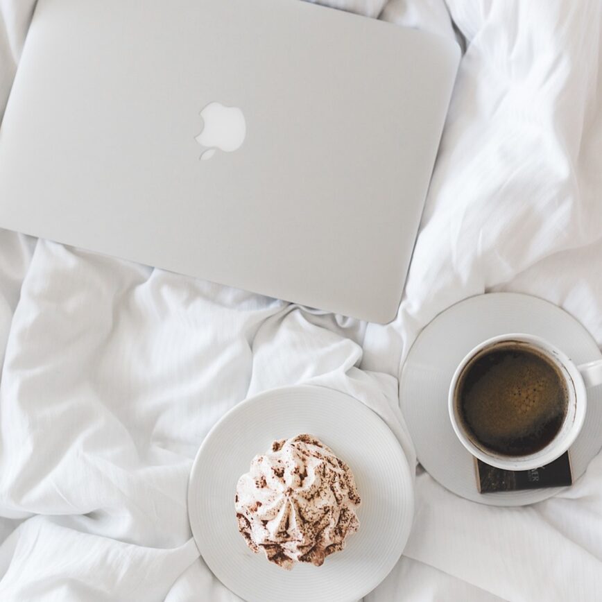 laptop on a bed with a coffee and baked good